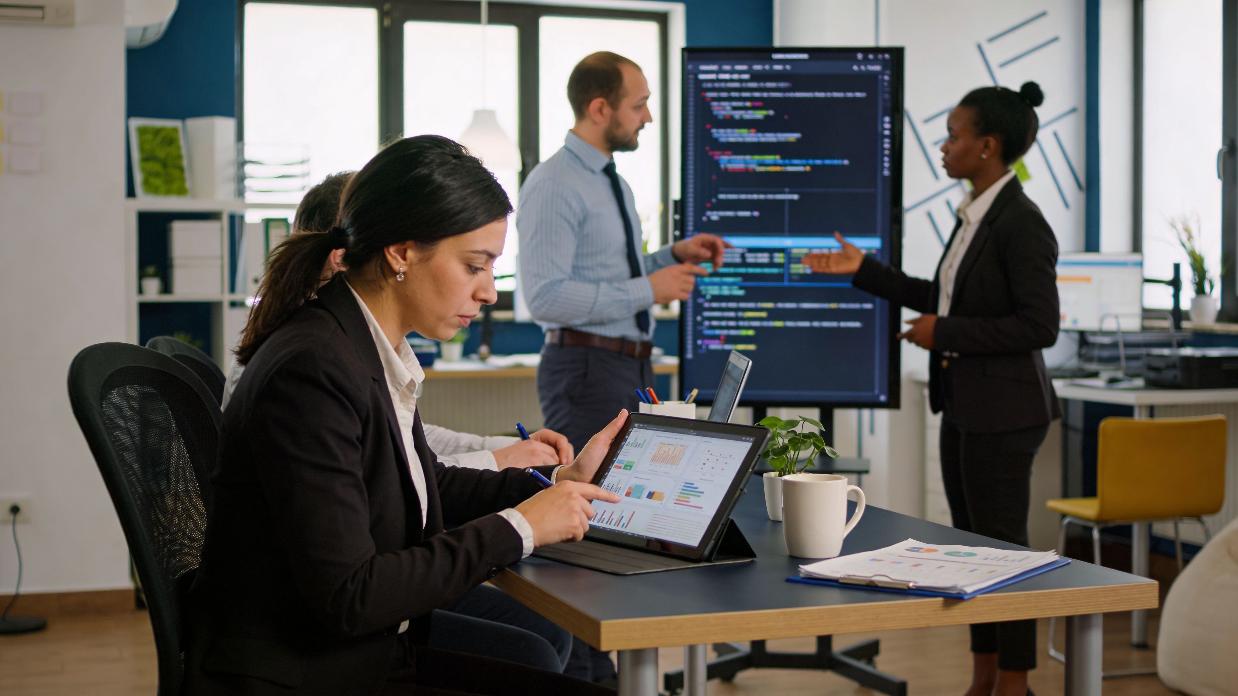 Profesionales de negocios analizando datos en una tableta durante una reunión corporativa en una oficina moderna y colaborativa.